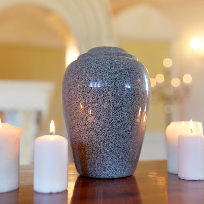 Funeral, cremation and mourning concept - funerary urn and candles on table burning in church